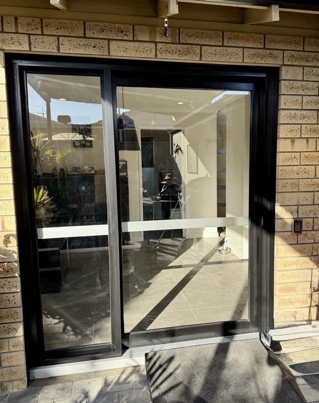 Black automatic sliding glass door installed in a brick home